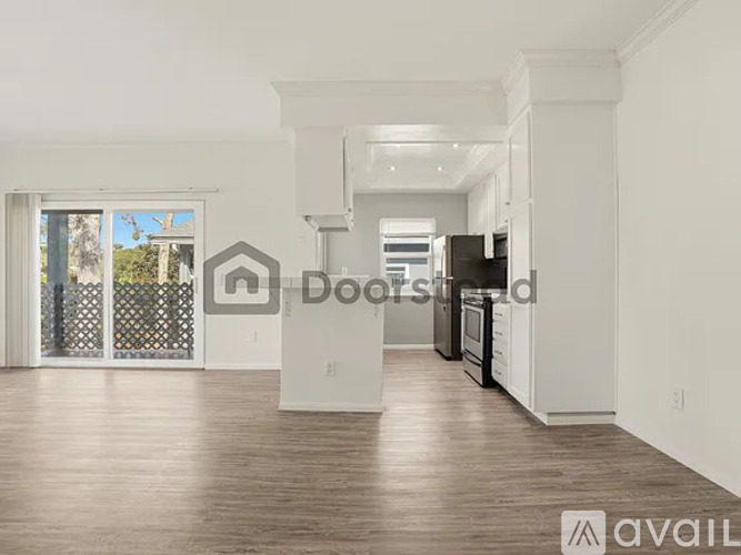 A large, empty, and well-lit kitchen and living room with hardwood floors and white walls.