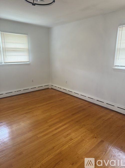 A room with wooden flooring and two windows.
