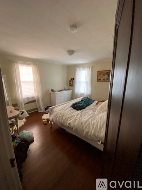 A bedroom with a white bed and a window with curtains.