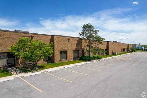 A parking lot in front of a brick building with a tree on the left.