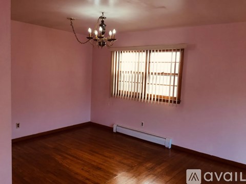 A room with a chandelier, wooden floor, and a window with blinds.
