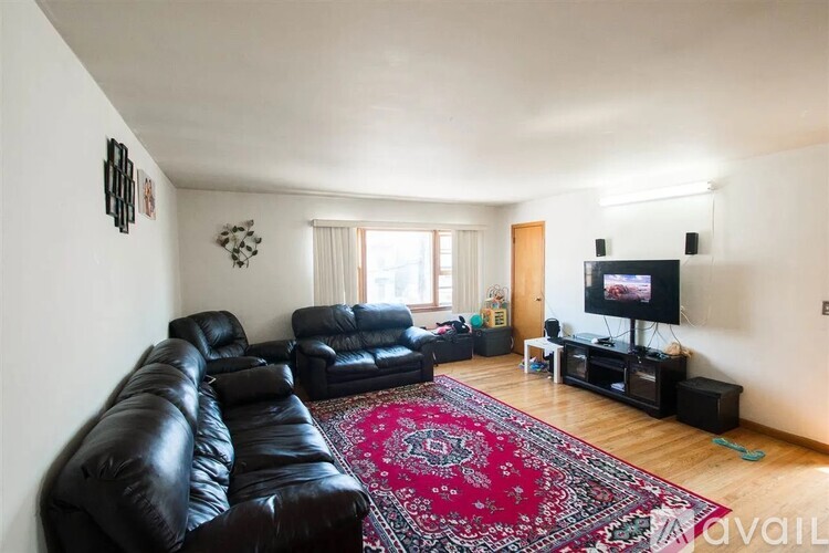 A living room with a black leather couch and a red rug.