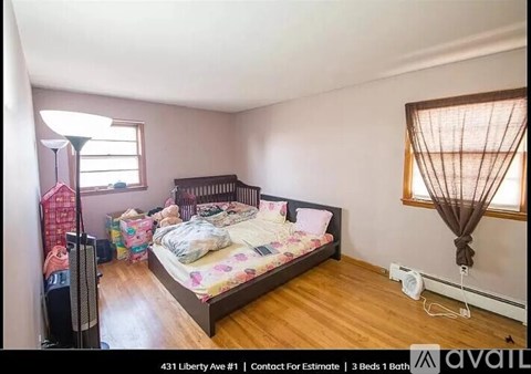 A bedroom with a bed, a window with curtains, and a wooden floor.