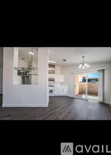 A spacious room with white walls and wooden flooring, featuring a kitchen area with white cabinets and a dining table.