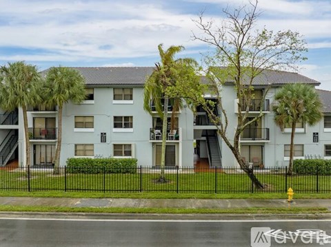 A white apartment building with a black fence in front.
