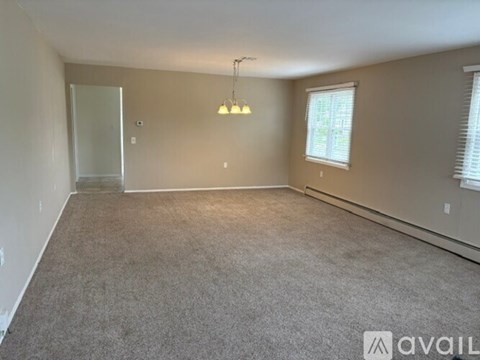 A spacious room with a carpeted floor, a window with blinds, and a hanging light fixture.