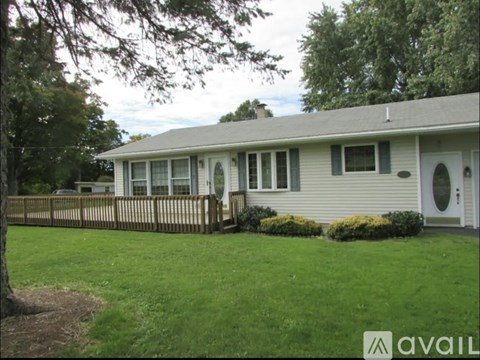 A house with a white door and windows is surrounded by a green lawn and trees.
