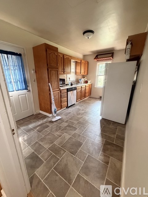 A kitchen with a white fridge, wooden cabinets, and a tiled floor.