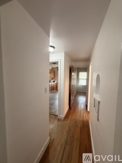 A hallway with wooden floors and white walls leading to a door.
