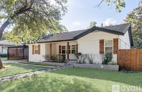 A house with a white exterior and a black roof is surrounded by a wooden fence and greenery.