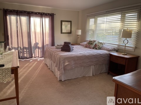 A bedroom with a large bed and a window with blinds.