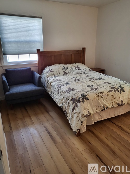 A bedroom with a bed, a chair, and a window with blinds.
