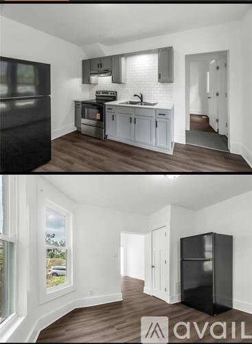A black refrigerator in a kitchen with white cabinets and a window.