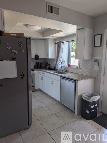 A kitchen with a refrigerator, cabinets, and a trash can.