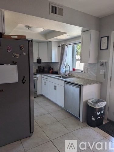 A kitchen with a refrigerator, cabinets, and a trash can.