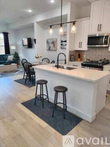 A kitchen with white cabinets and a white island with two black stools.
