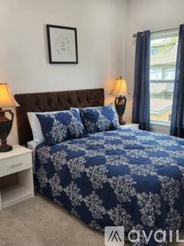 A bed with a dark blue floral comforter and matching pillows sits in a room with a white nightstand and lamp.