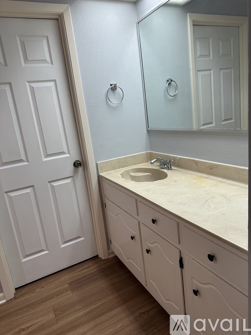 A bathroom with a white door, sink, and cabinets.