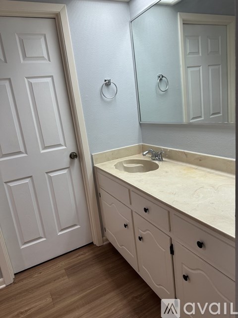 A bathroom with a white door, sink, and cabinets.
