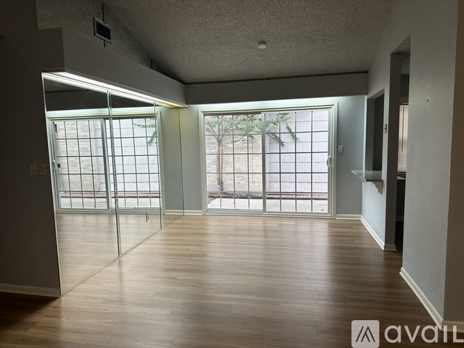 A spacious room with wooden floors and sliding glass doors leading to a balcony.