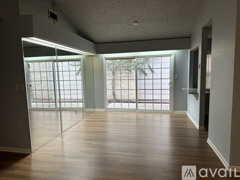 A spacious room with wooden floors and sliding glass doors leading to a balcony.