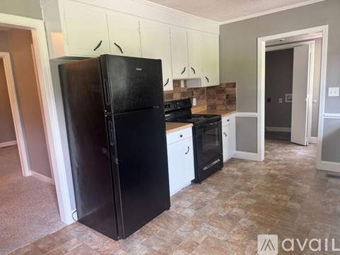 A black refrigerator stands in a kitchen with white cabinets and a tiled backsplash.