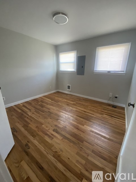 A room with wooden flooring and two windows.