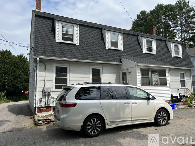 A white car is parked in front of a two-story house.