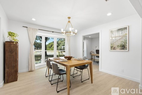 A dining room with a wooden table and chairs, a chandelier, and a view of the backyard through the sliding glass doors.