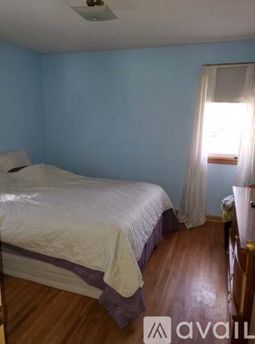 A bedroom with a bed, wooden floors, and a window with curtains.