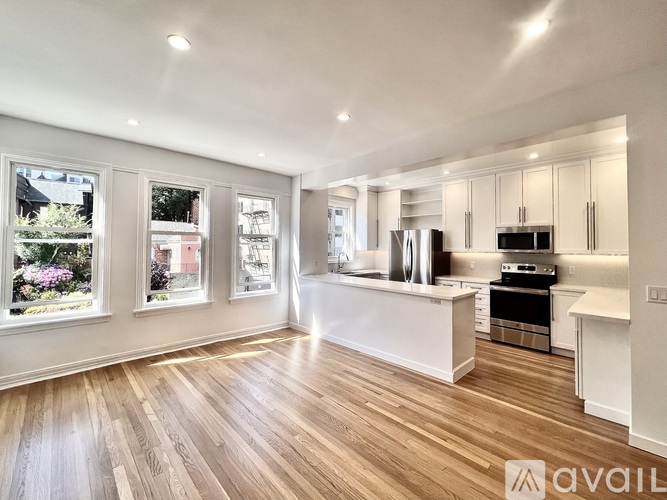 A spacious kitchen with wooden floors and white cabinetry.