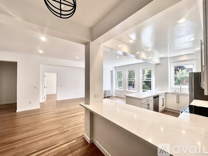 A spacious kitchen with a long white countertop and wooden flooring.