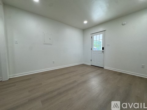 A room with a white door and a window, with a wooden floor and white walls.