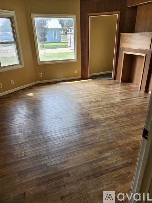 A room with wooden flooring and a window overlooking a blue house.