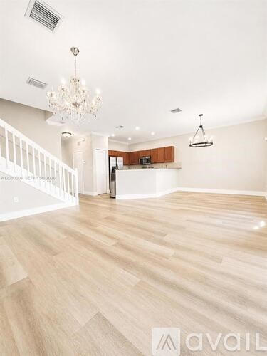 A spacious room with wooden flooring and a chandelier hanging from the ceiling.