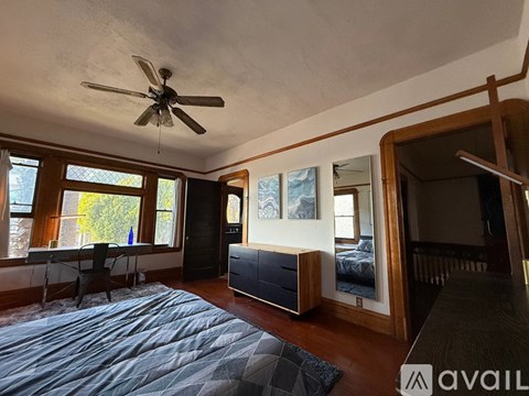 A bedroom with a bed, a chair, a ceiling fan, and a large window.