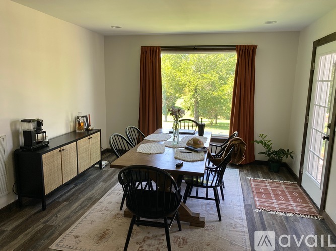 A dining room with a table set for two and a view of a tree-filled yard through the window.