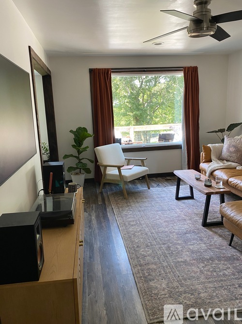 A living room with a brown sofa, a white chair, a wooden cabinet, and a ceiling fan.