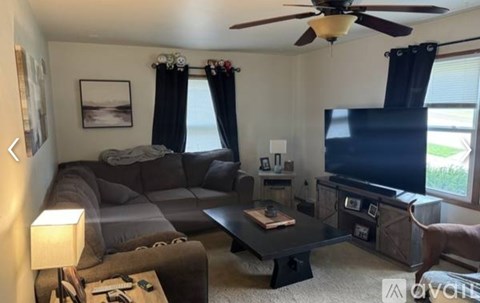 A living room with a grey couch, a black coffee table, a flat screen TV, and a ceiling fan.