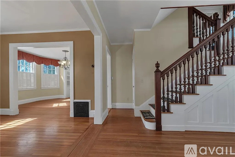 A spacious hallway with a staircase and a window with red curtains.