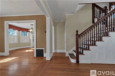 A spacious hallway with a staircase and a window with red curtains.