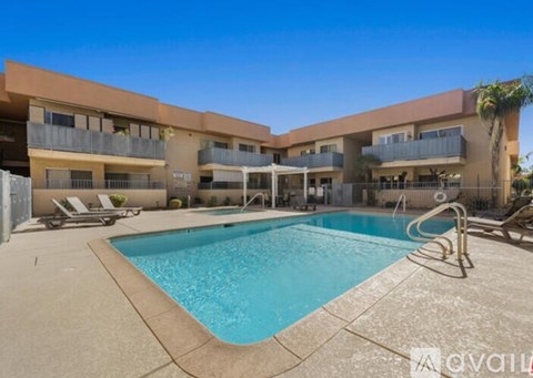 A large swimming pool is surrounded by a concrete patio and lounge chairs.
