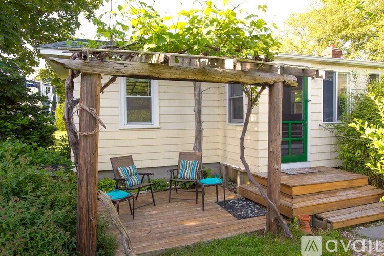 A wooden pergola with a green door and two chairs on a wooden deck.