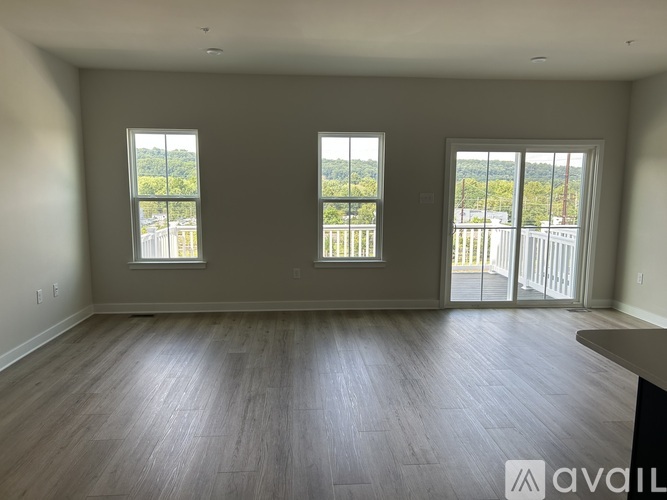 A spacious room with wooden flooring and three windows.