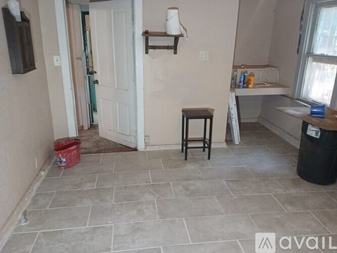 A room with a white door, a small table, and a red bucket on the floor.