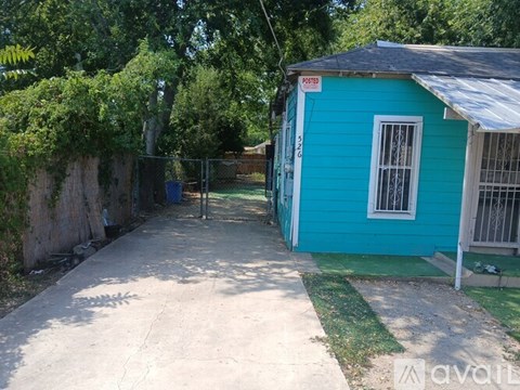 A blue shed with a white door and window is surrounded by a concrete path and greenery.
