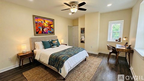 A bedroom with a bed, a ceiling fan, and a painting on the wall.