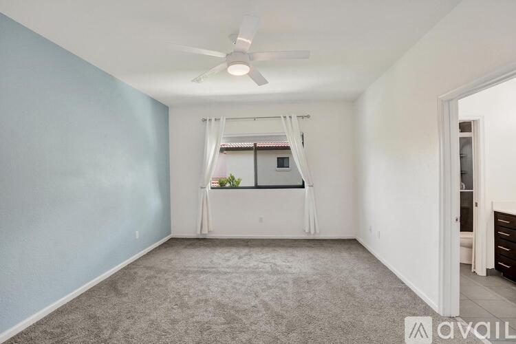A room with a ceiling fan and a window with a view of a building.