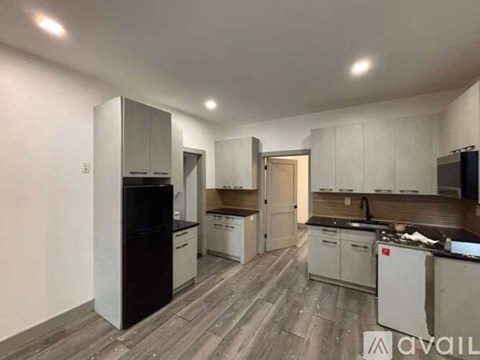 A kitchen with a black fridge, white cabinets, and a wooden floor.