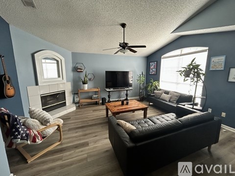 A living room with a black couch, a wooden chair, a fireplace, and a ceiling fan.